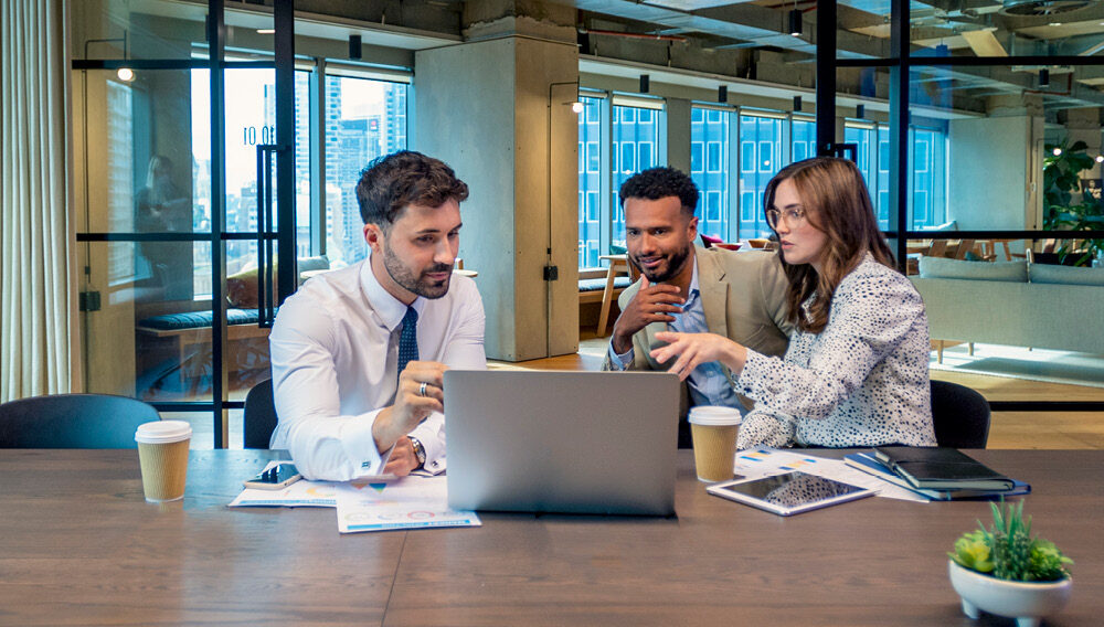 Three colleagues are seated around a table in a modern office