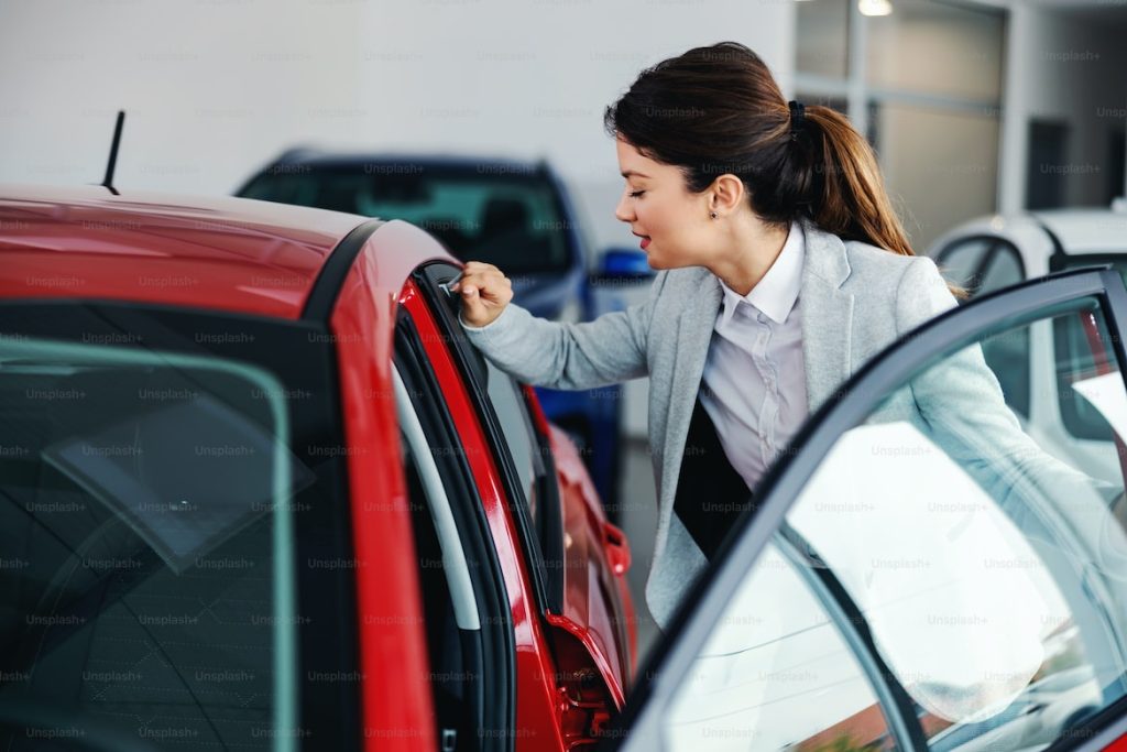 A woman is inspecting the interior of a red car