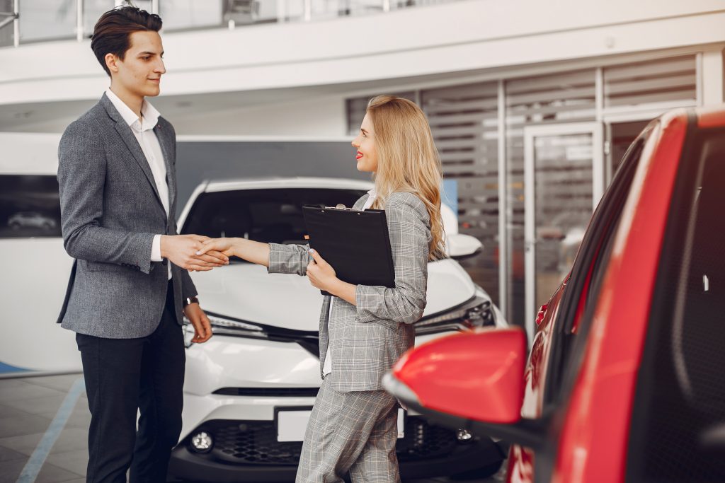 A man and a woman are shaking hands in a car dealership.