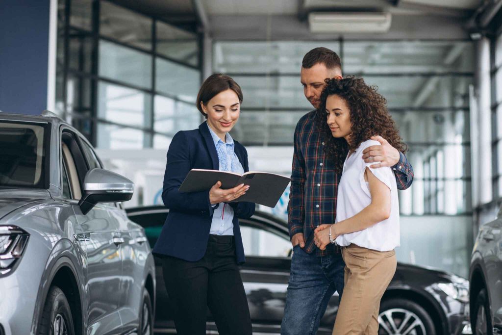 A car salesperson shows a couple a brochure at car dealership